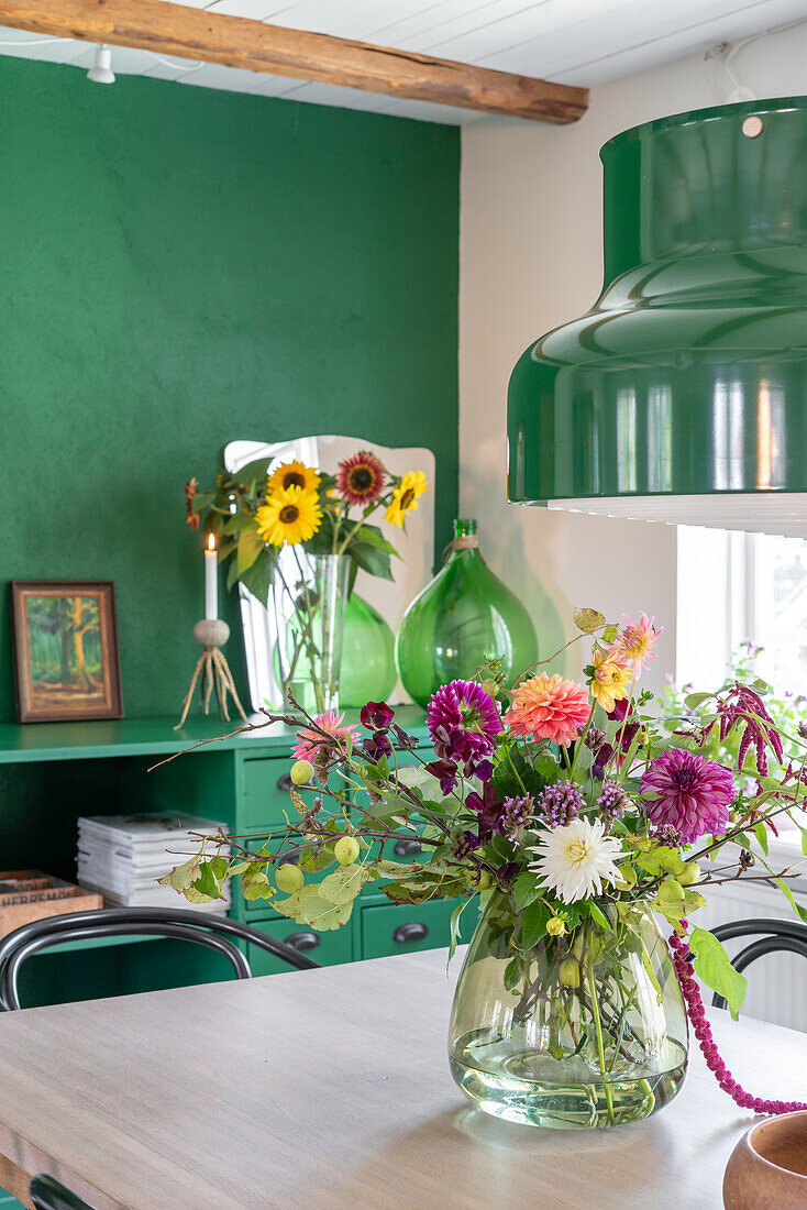 Colourful bouquet of flowers on wooden table, green wall and pendant light