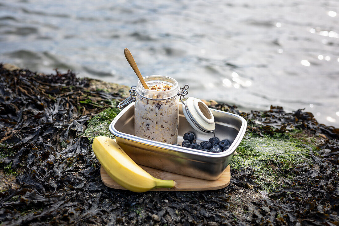 Overnight Oats with blueberries in a lunchbox and a banana on the bank
