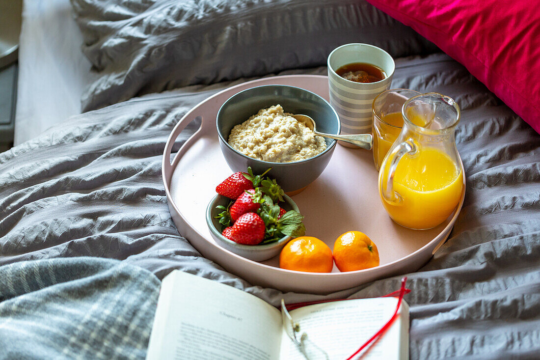 Frühstückstablett mit Porridge, Tee, Orangensaft und Obst auf Bett