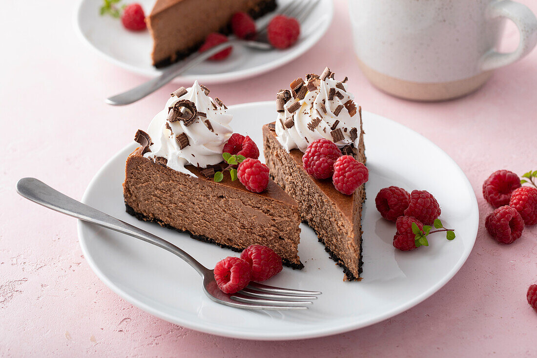 Chocolate cheesecake with cookie base topped with whipped cream, fresh raspberry and chocolate shavings