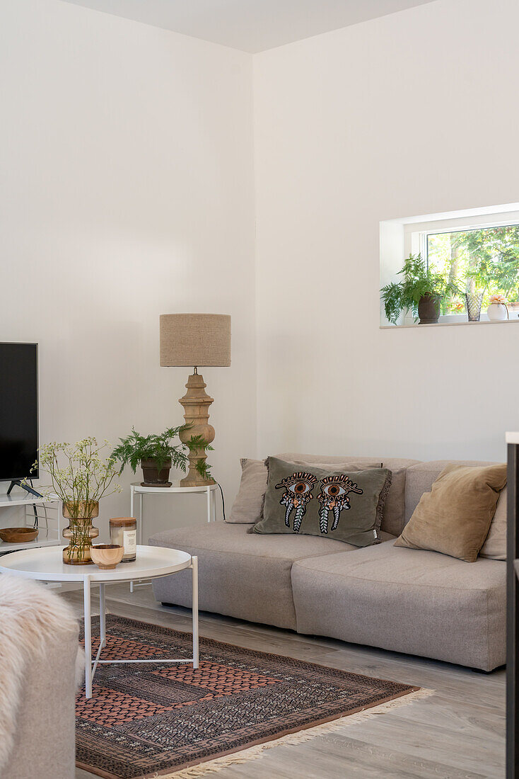 Living room with sofa in beige, plants and patterned carpet