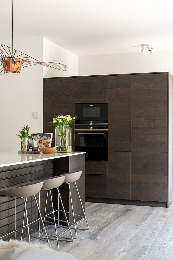 Kitchen island with bar stools and kitchen cabinets with integrated electrical appliances