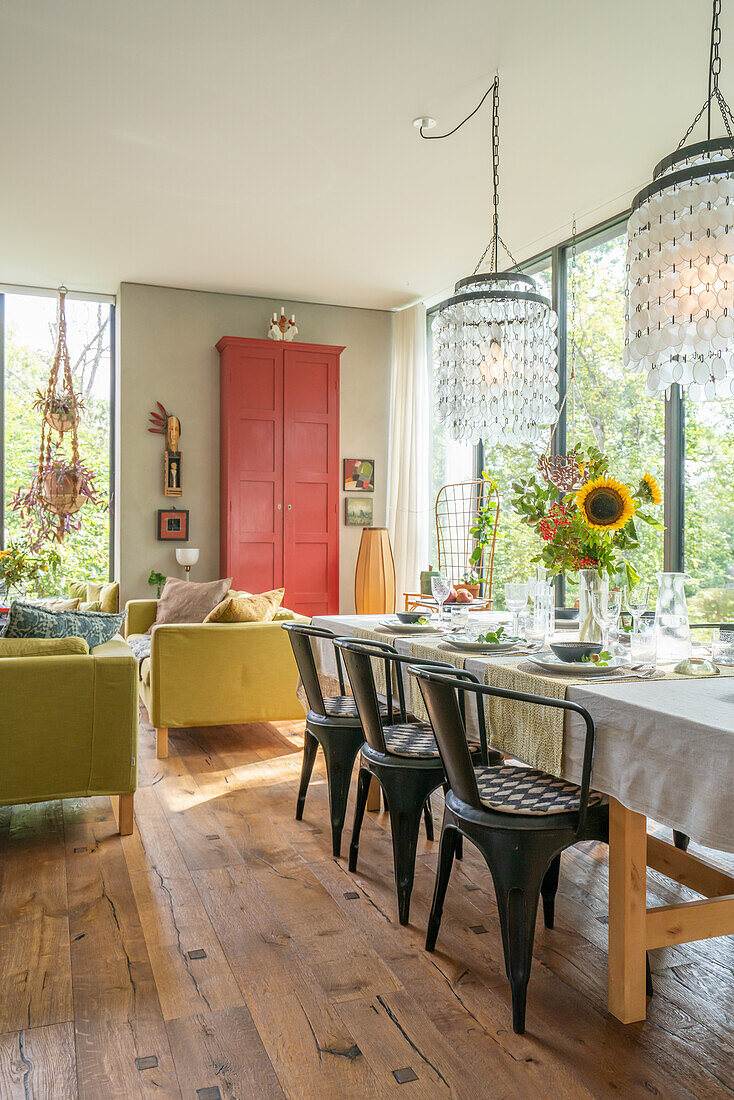 Gedeckter Esstisch mit Blumenstrauß, Hängeleuchten und roter Schrank