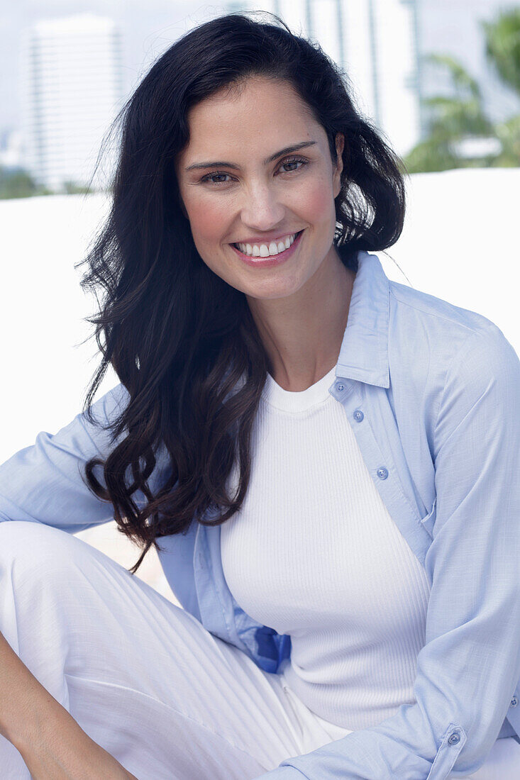A dark-haired woman wearing a white top, a light-blue shirt and white trousers