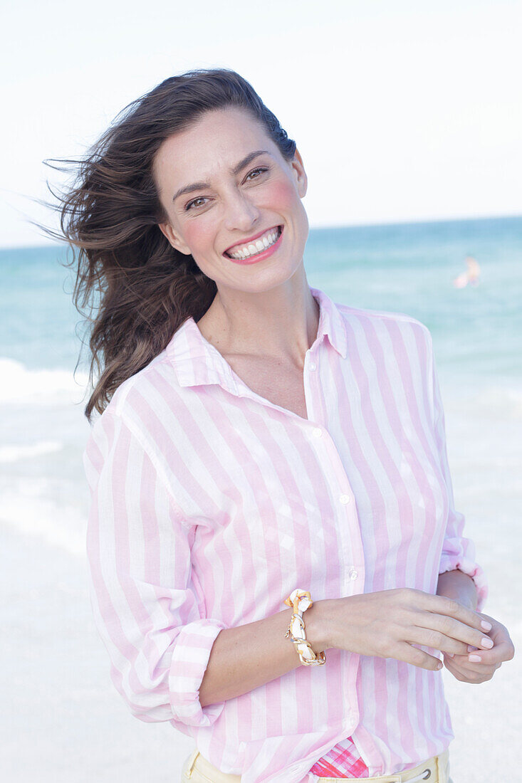 Brünette Frau in rosa gestreifter Bluse am Strand