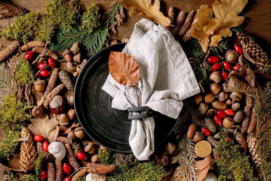 Empty black ceramic plate with cloth napkin over ambiance magic autumnal forest background