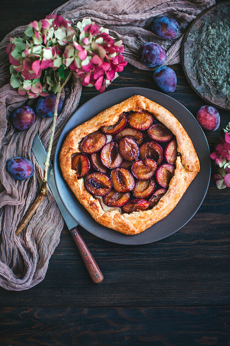 Pflaumen-Galette umgeben von frischen Pflaumen und Hortensie