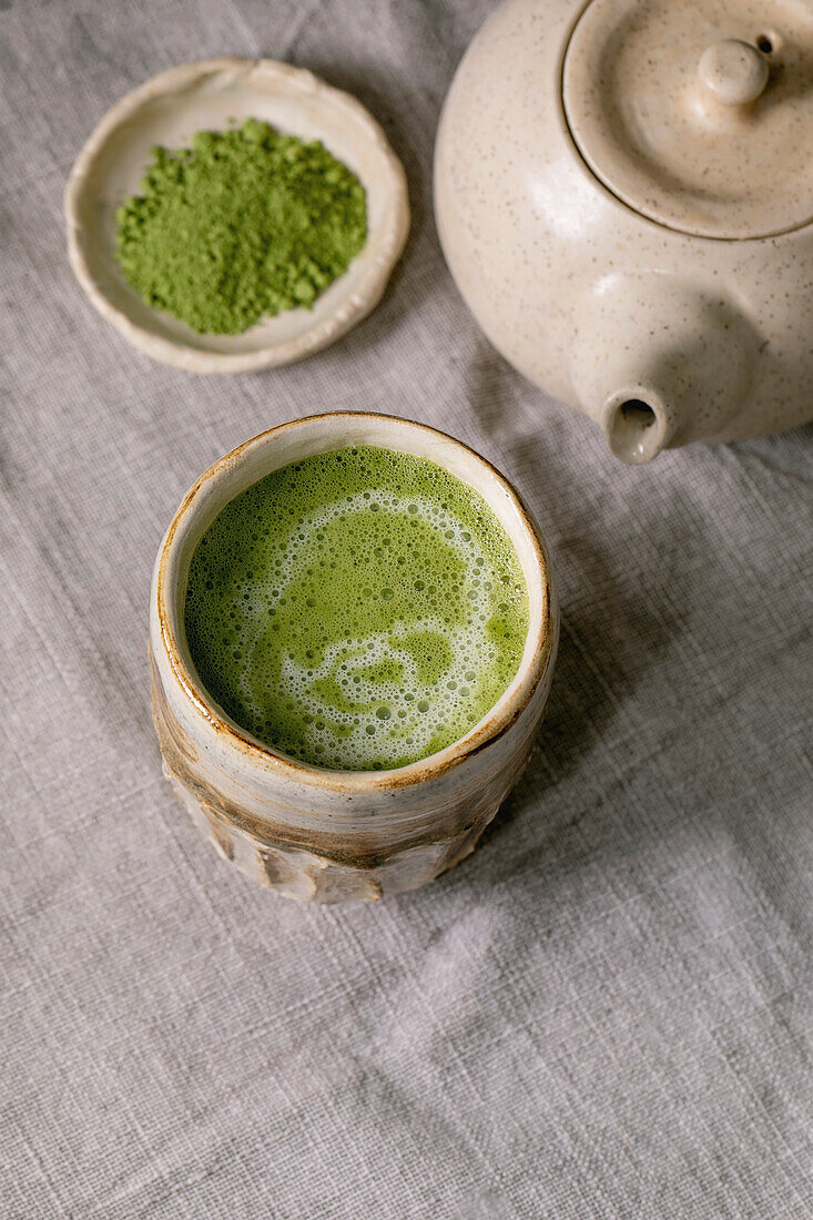 Traditional japanese hot green frothy tea matcha latte in handmade ceramic cup, powdered matcha and teapot