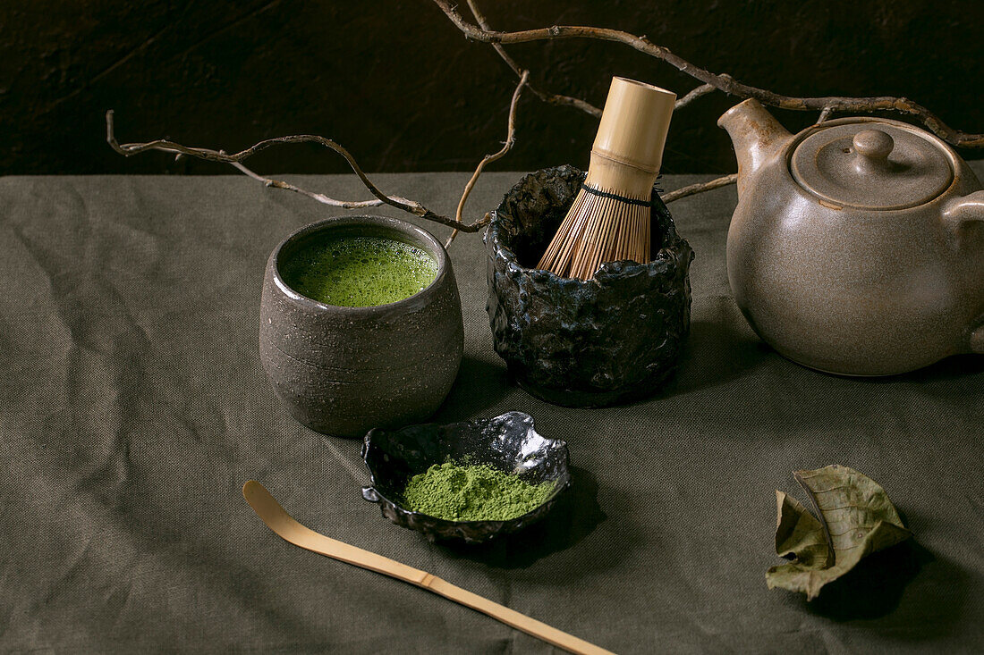 Traditional japanese hot green frothy tea matcha in craft ceramic cup, powdered matcha, teapot and bamboo whisk