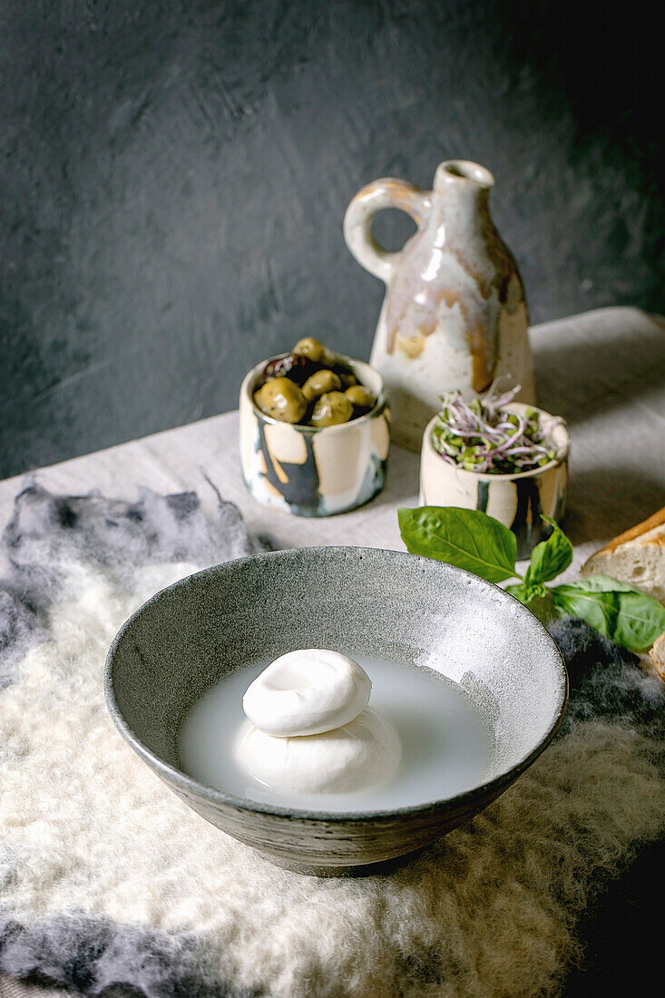 Traditional italian burrata knotted cheese in brine in grey ceramic bowl on table