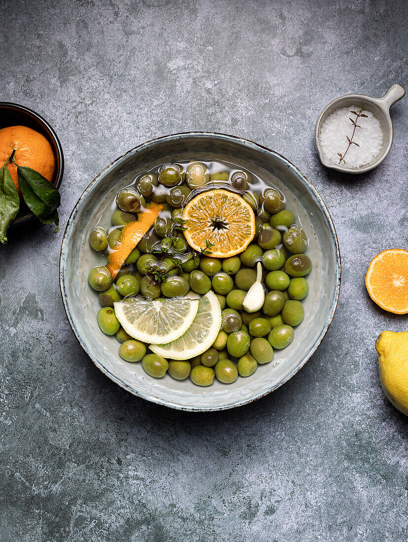 Bowl with olives in brine served with sliced lemon placed on gray table in restaurant