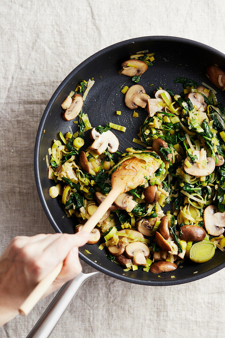 Champignons, Lauch und Spinat in einer Pfanne anbraten