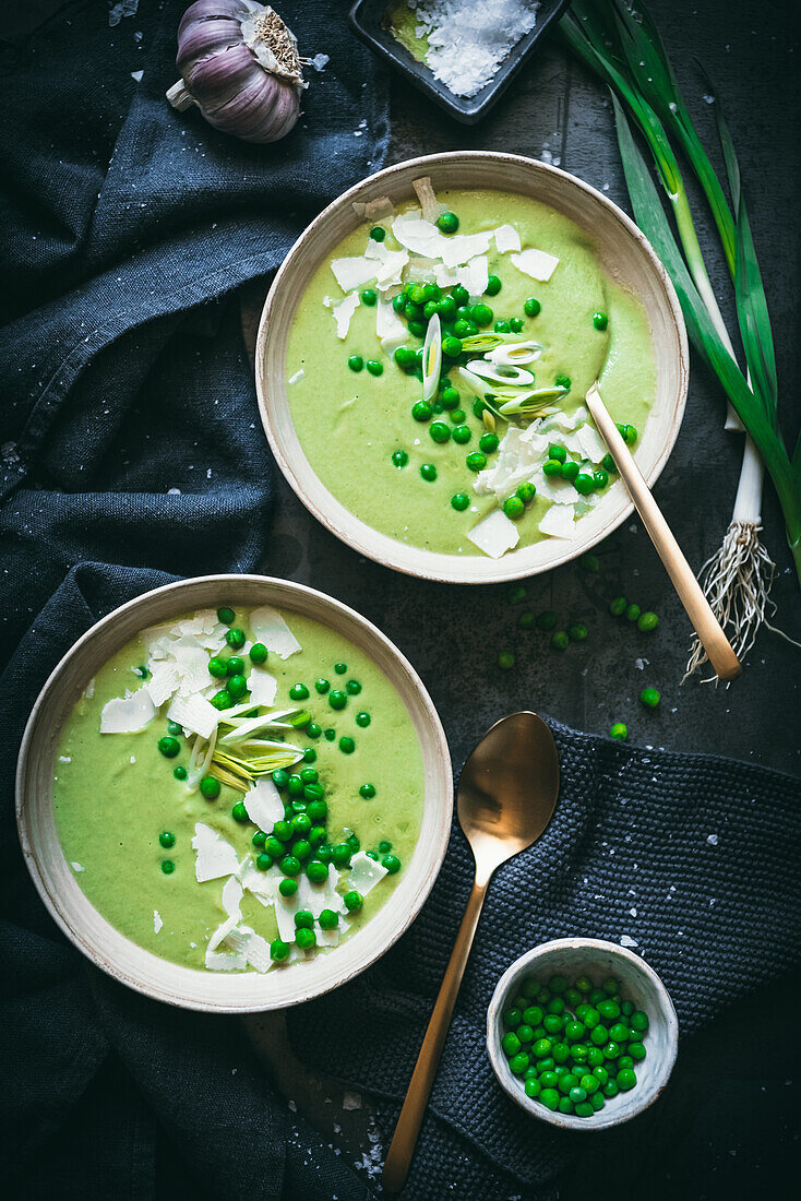 Bowls with creamy pea soup served on table with black napkins and green onion