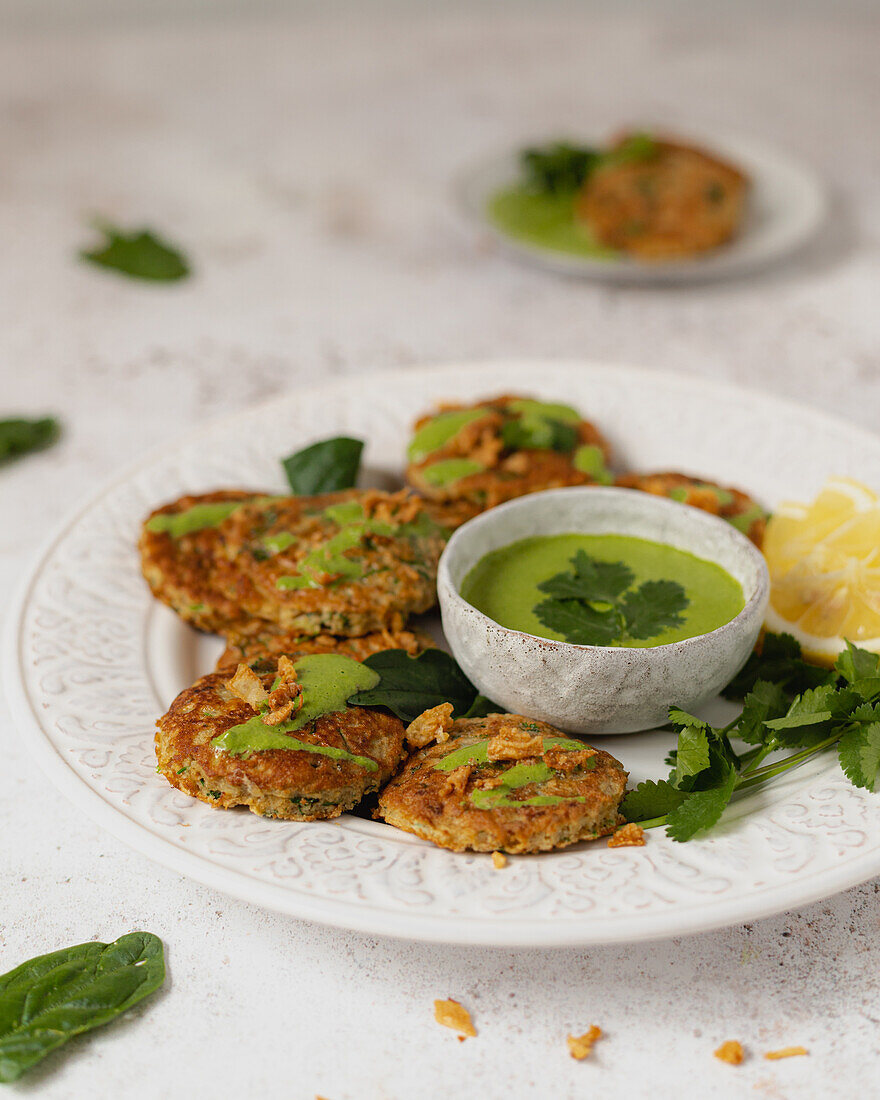 Herbal fritters garnished with healthy green sauce parsley and lemon slices on white table
