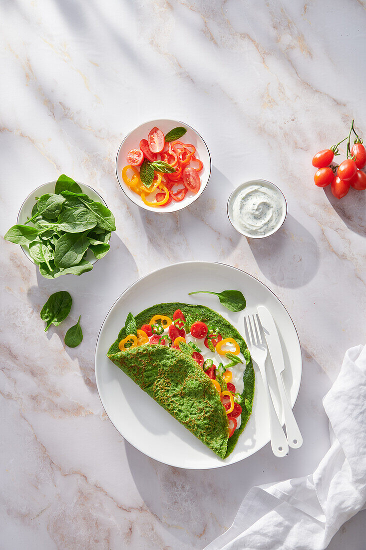 Spinach creppe with tomato and pepper slices and sour cream