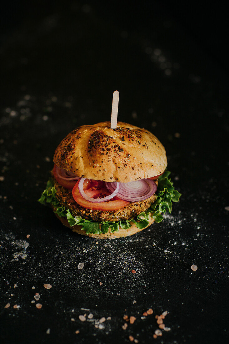 Vegan burger with fresh ripe vegetables served on black background in studio