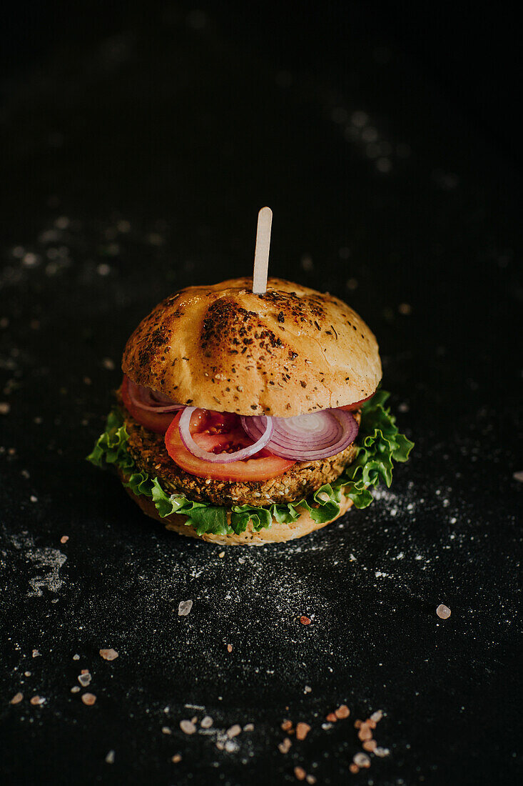Veganer Burger mit frischem Gemüse auf schwarzem Untergrund