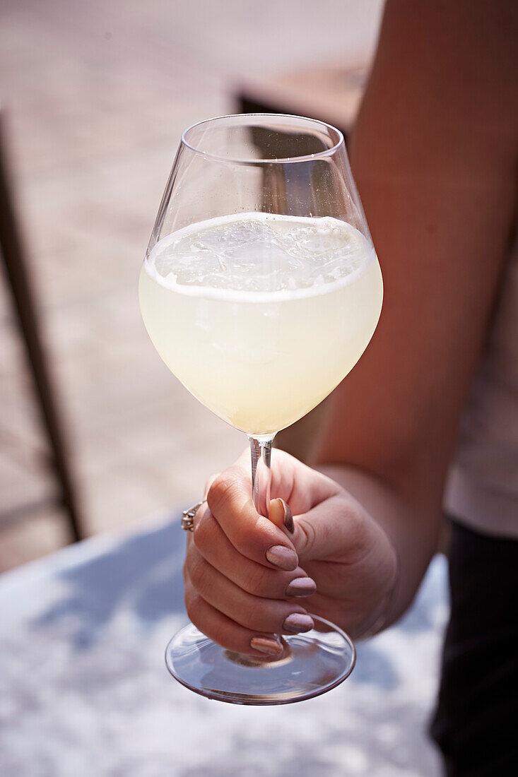 A hand holding a lemonny summer drink in a stemmed glass