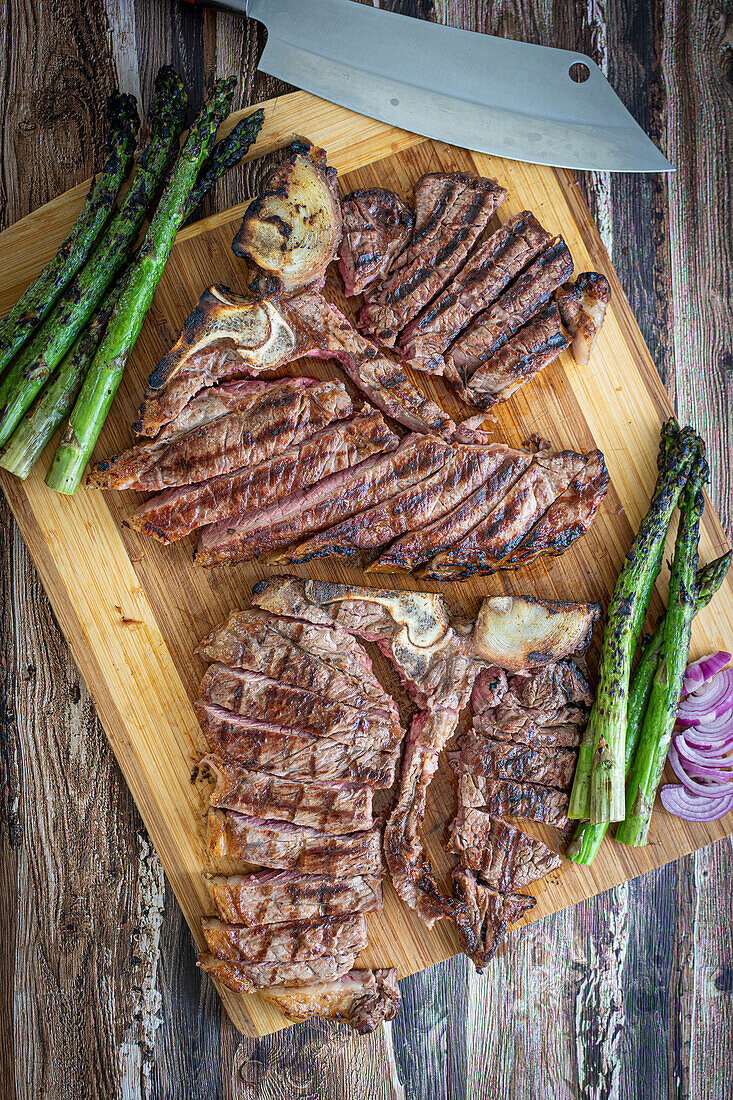 Gegrillte T-Bone-Steaks mit grünem Spargel auf Holzbrett