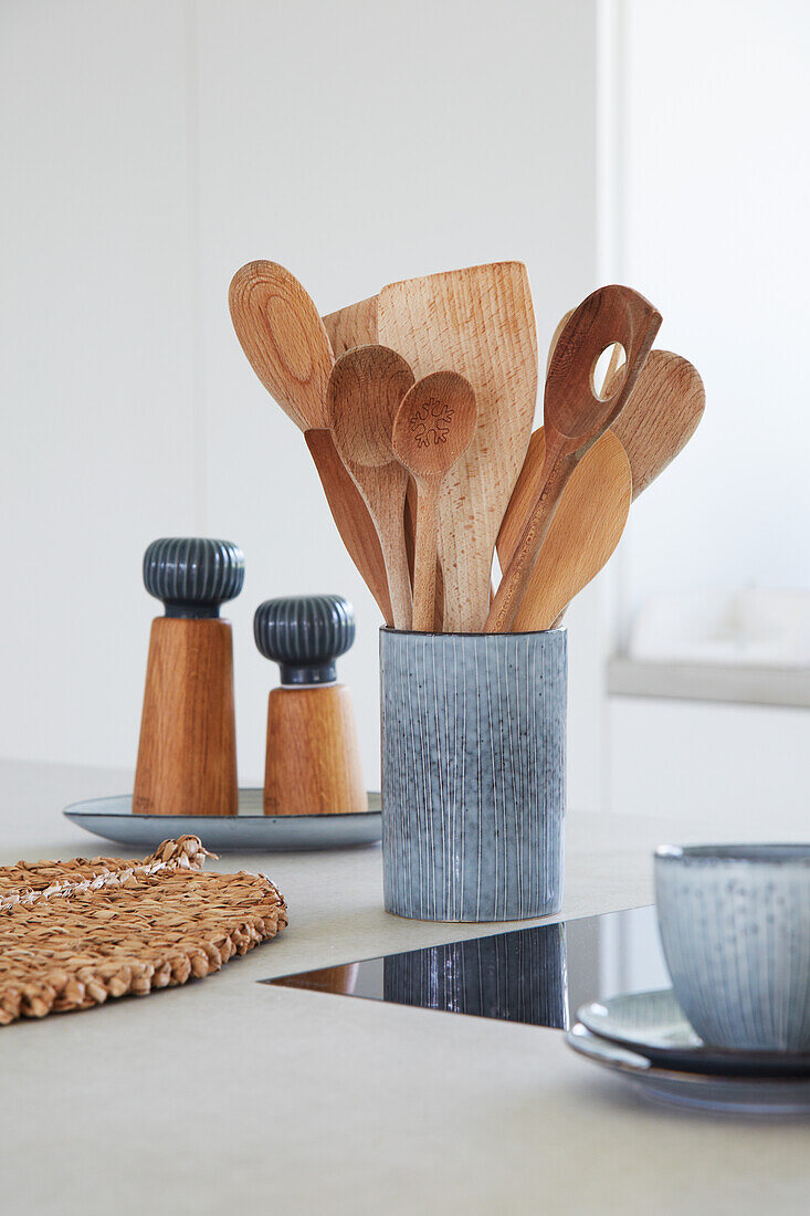 Wooden spoons in ceramic vase next to salt and pepper mills on kitchen worktop