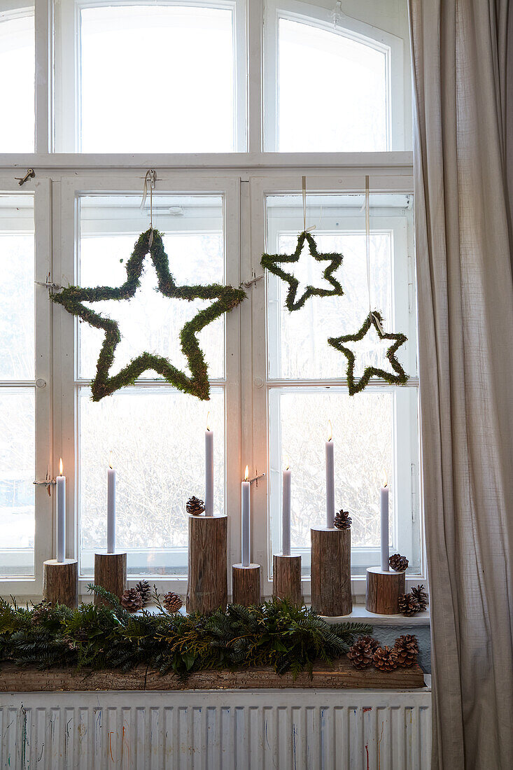 Hängende Sternen aus Moos, Kerzen und Tannenzweige als weihnachtliche Fensterdekoration