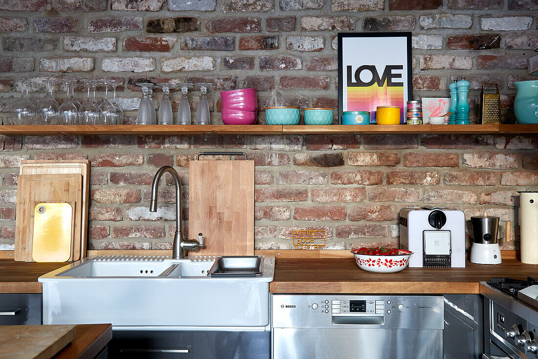 Wooden shelf with colorful bowls above kitchen worktop on brick wall