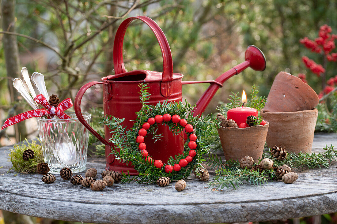 Christmas arrangement with red watering can, pine branches, ornamental apples, and clay pots