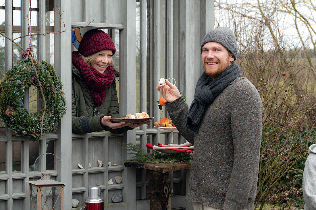 Woman handing man Christmas cookies through the window