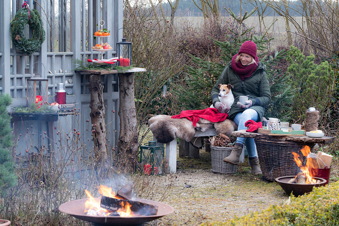 Cozy seat in the garden - woman with dog sitting on the bench, fire pit in the foreground