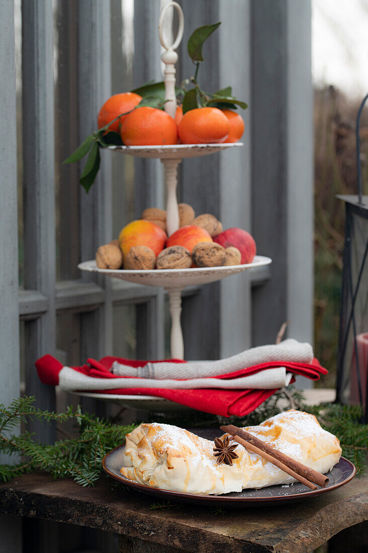 Curd filled strudel with star anise and cinnamon stick and tiered dessert stand with mandarins, apples, and walnuts