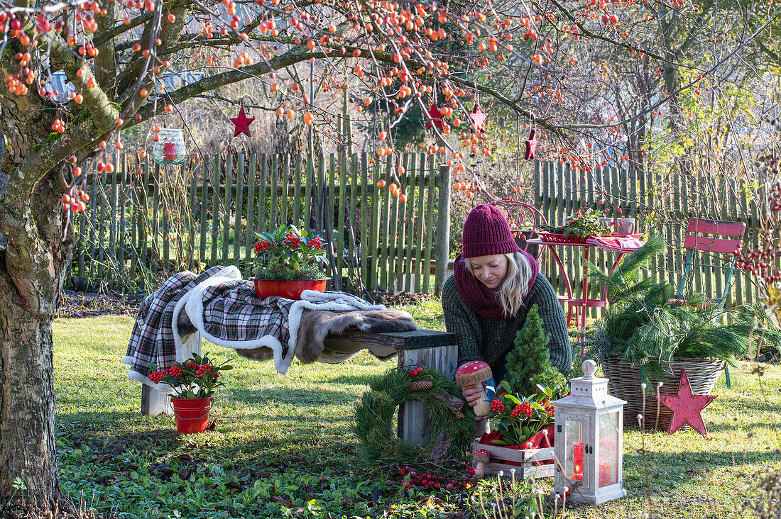 Woman decorating Christmas seat with lantern, mushrooms and wreath in the garden