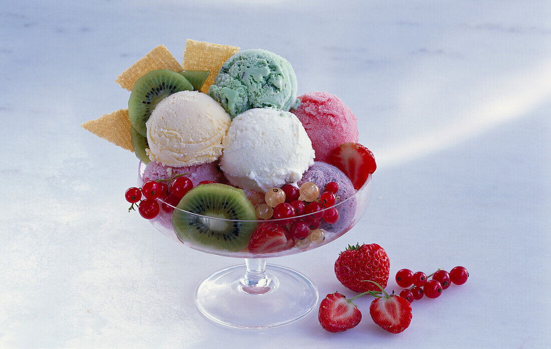 Ice cream scoops with fresh fruit and wafers in a glass dish