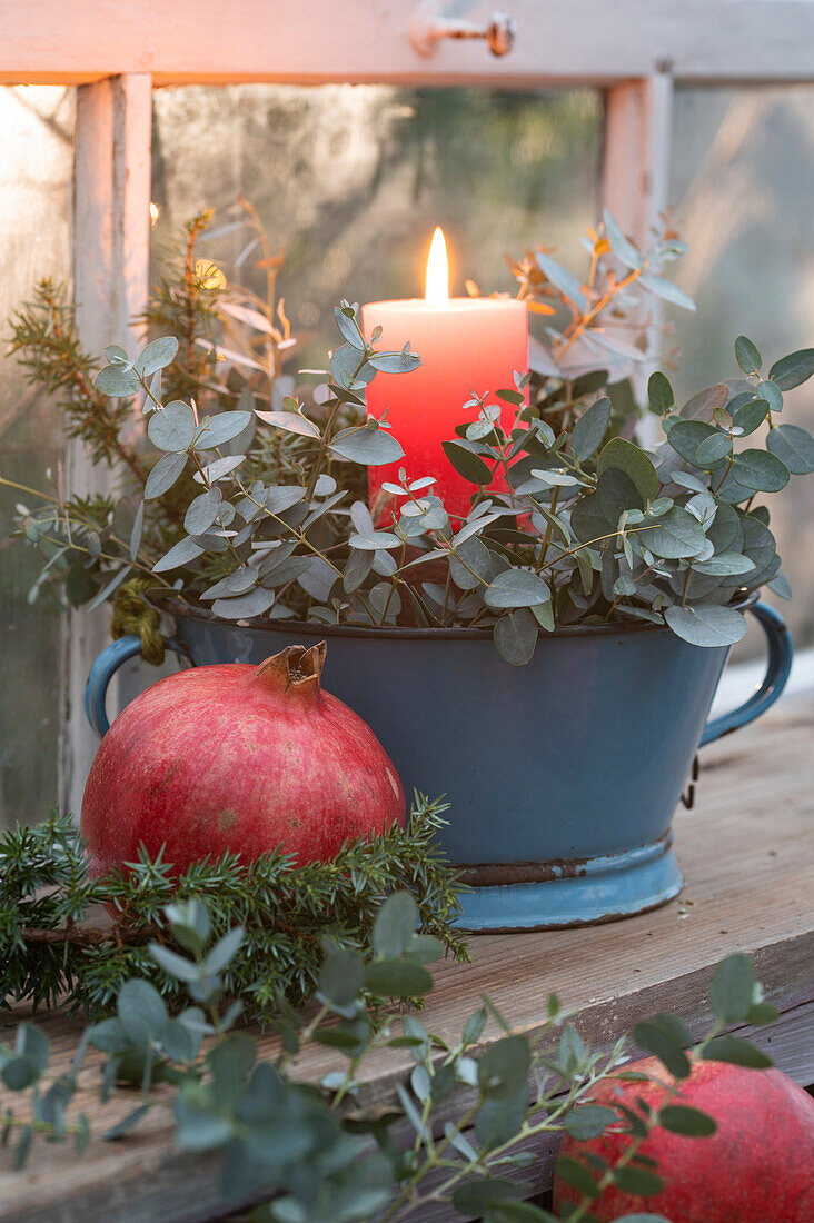 Vintage enamel bowl with eucalyptus and burning candle, in front pomegranate