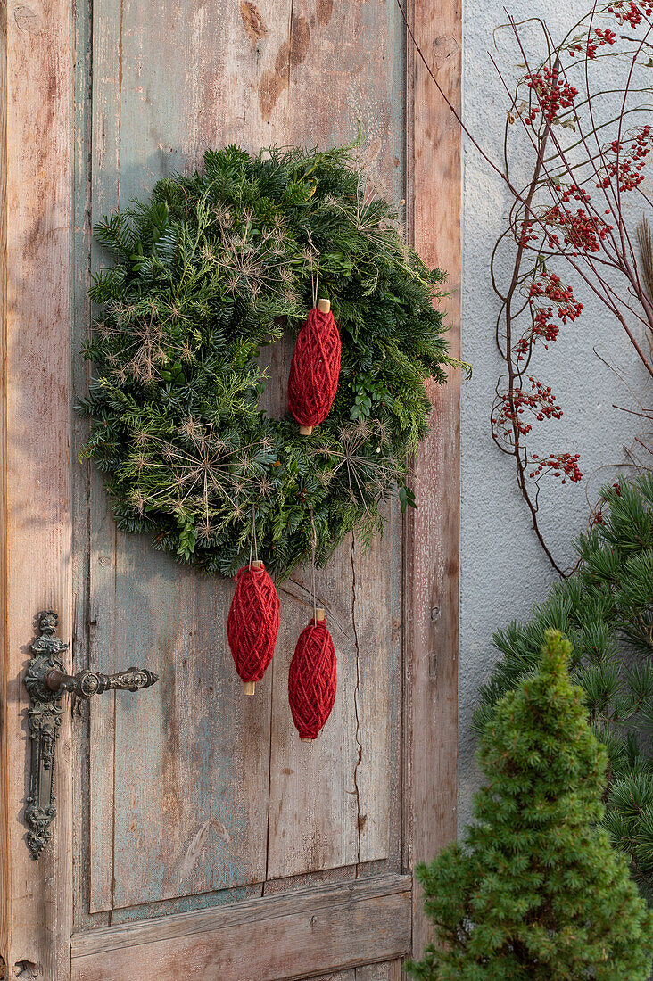 Door wreath made of conifer branches (Coniferales), fennel seed stand, and rolls of red yarn