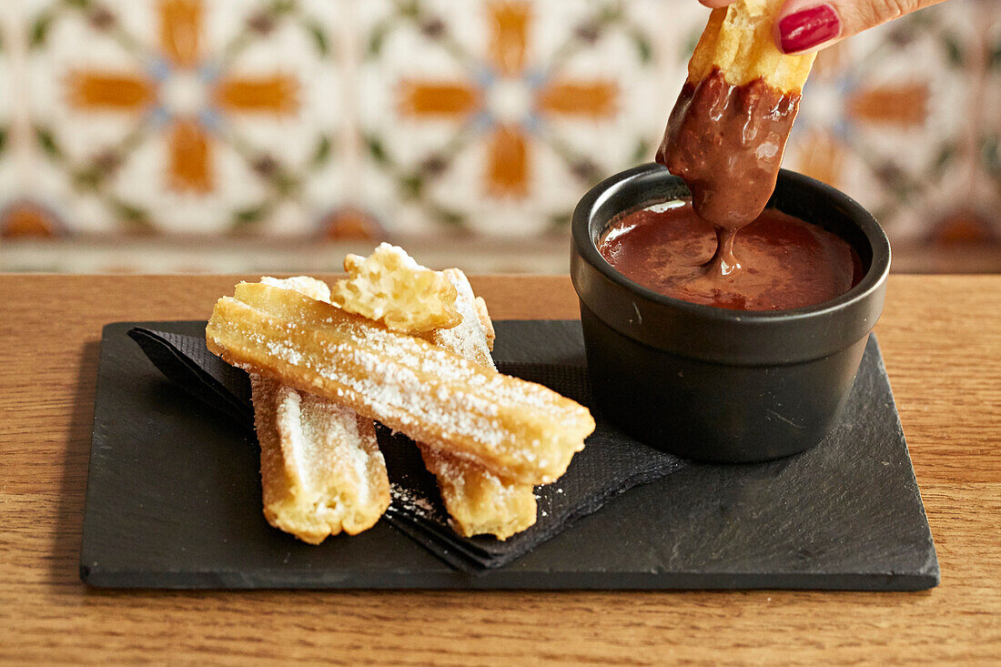 Churros being dipped in chocolate sauce