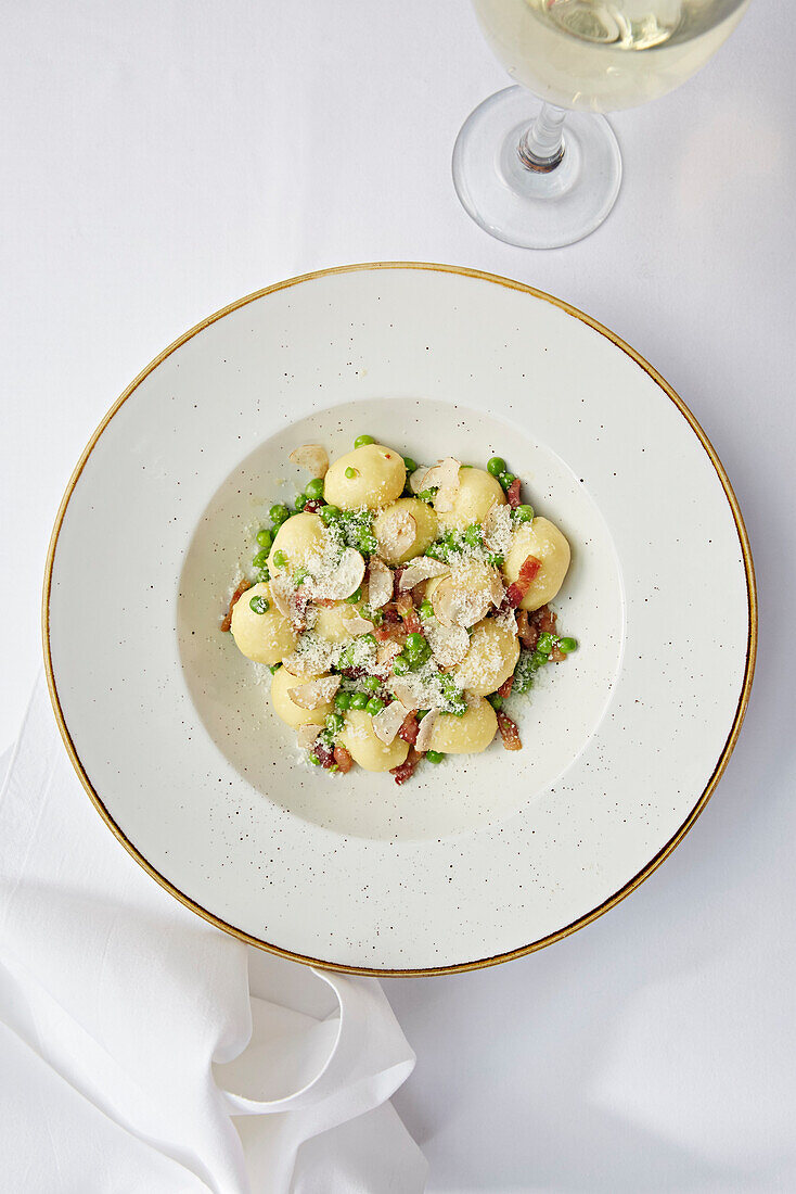 Gnocci mit geraspeltem Trüffel, Parmesan, Erbsen und Speck dazu ein Glas Weißwein