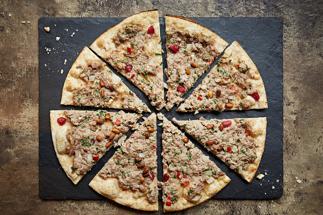 Pizza mit Schweinswurst, Granatapfelkernen und Pinienkernen, geschnitten auf Schieferplatte