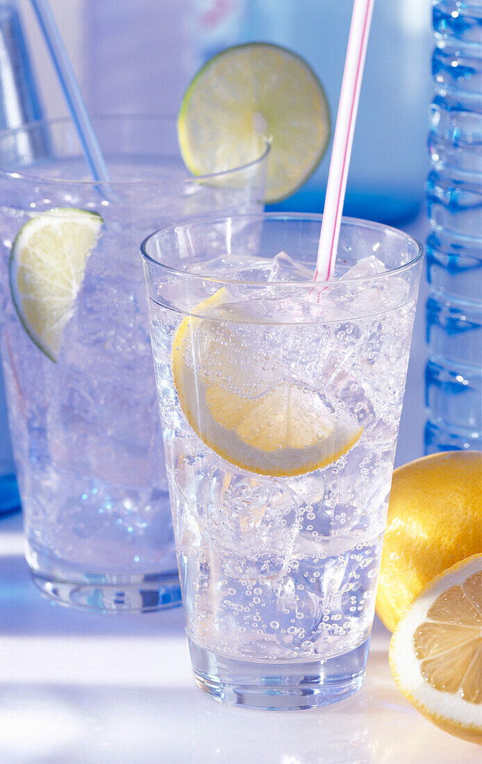 Two glasses of sparkling mineral water, straw, ice cubes, lemon, and lime