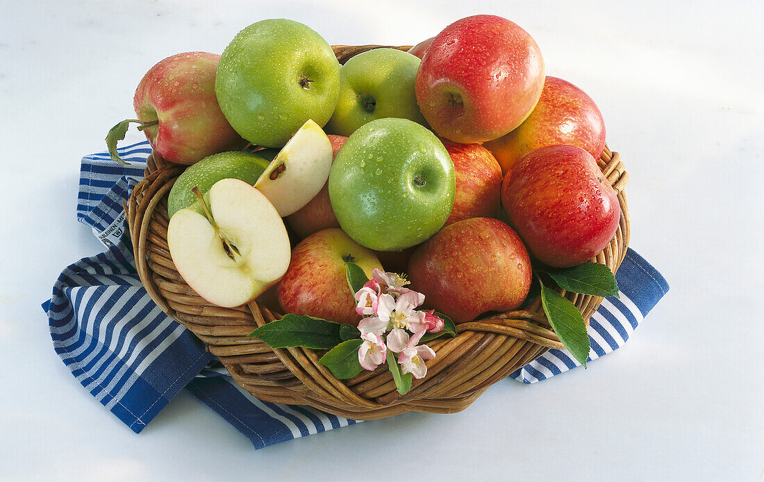 Kleiner Korb mit verschiedenen Äpfeln auf gestreiftem Tuch