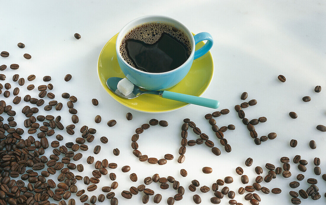 Eine bunte Tasse mit Kaffee, umgeben von Kaffeebohnen und Schriftzug 'Café'