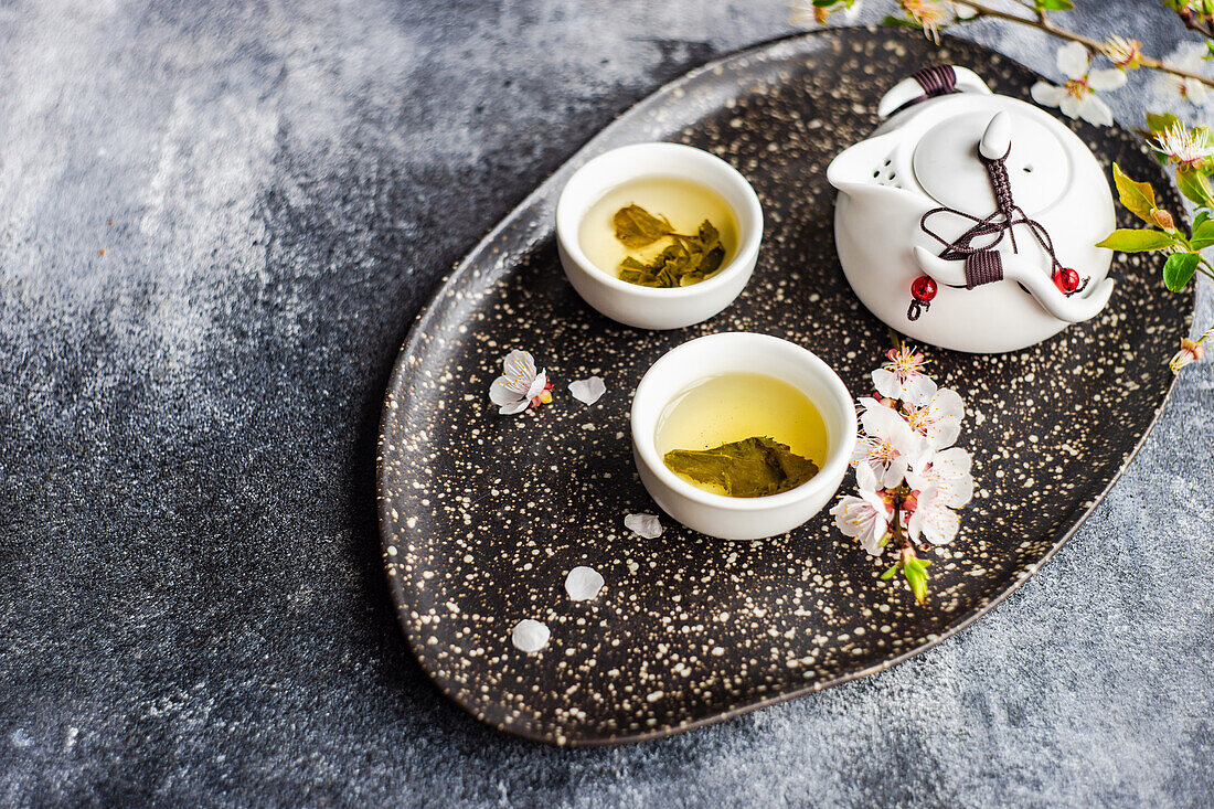 Green asian tea set on rustic background and decorated with blooming cherry tree