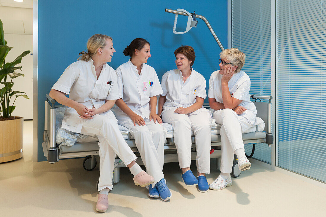 Group of nurses on hospital bed laughing and talking
