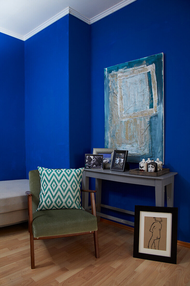 Upholstered chair with a throw pillow in front of console table and painting in a room with blue walls