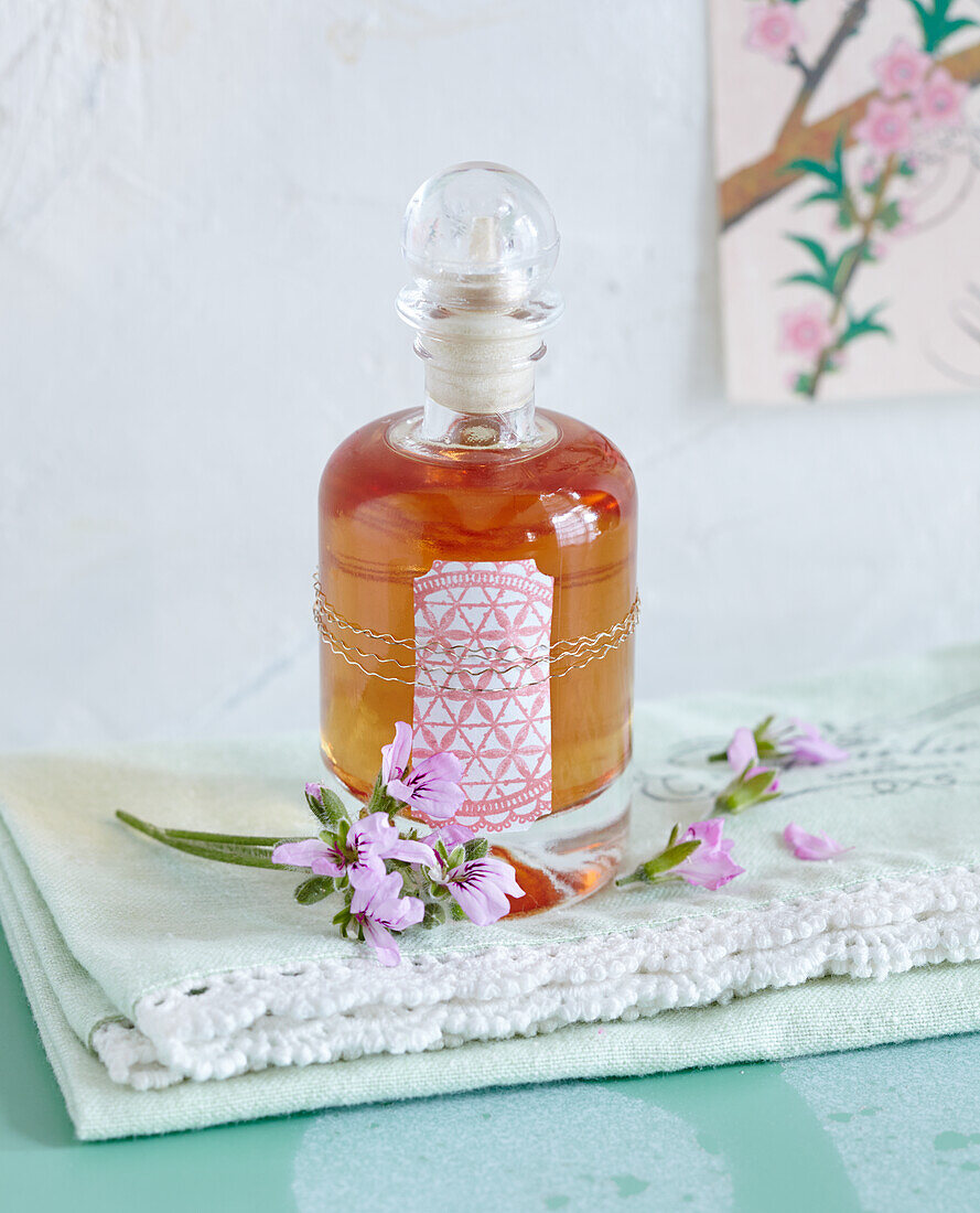 St. John's wort oil in a corked bottle, in front of it, geranium blossoms