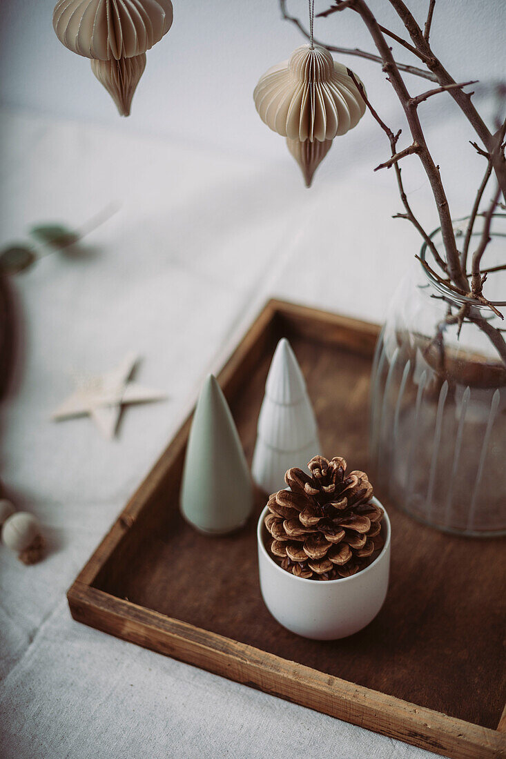 Decorative tray with cones, small ceramic fir trees and glass vase with twigs