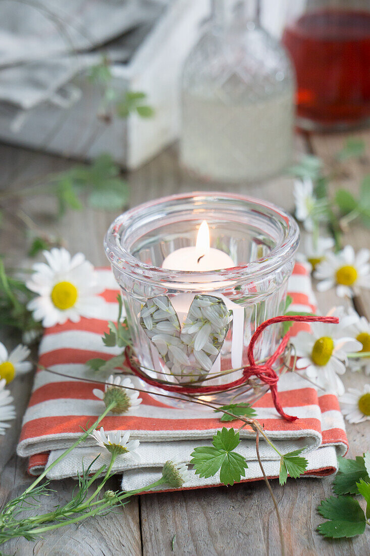 Glass lantern, decorated with a heart of chamomile blossoms and red rope