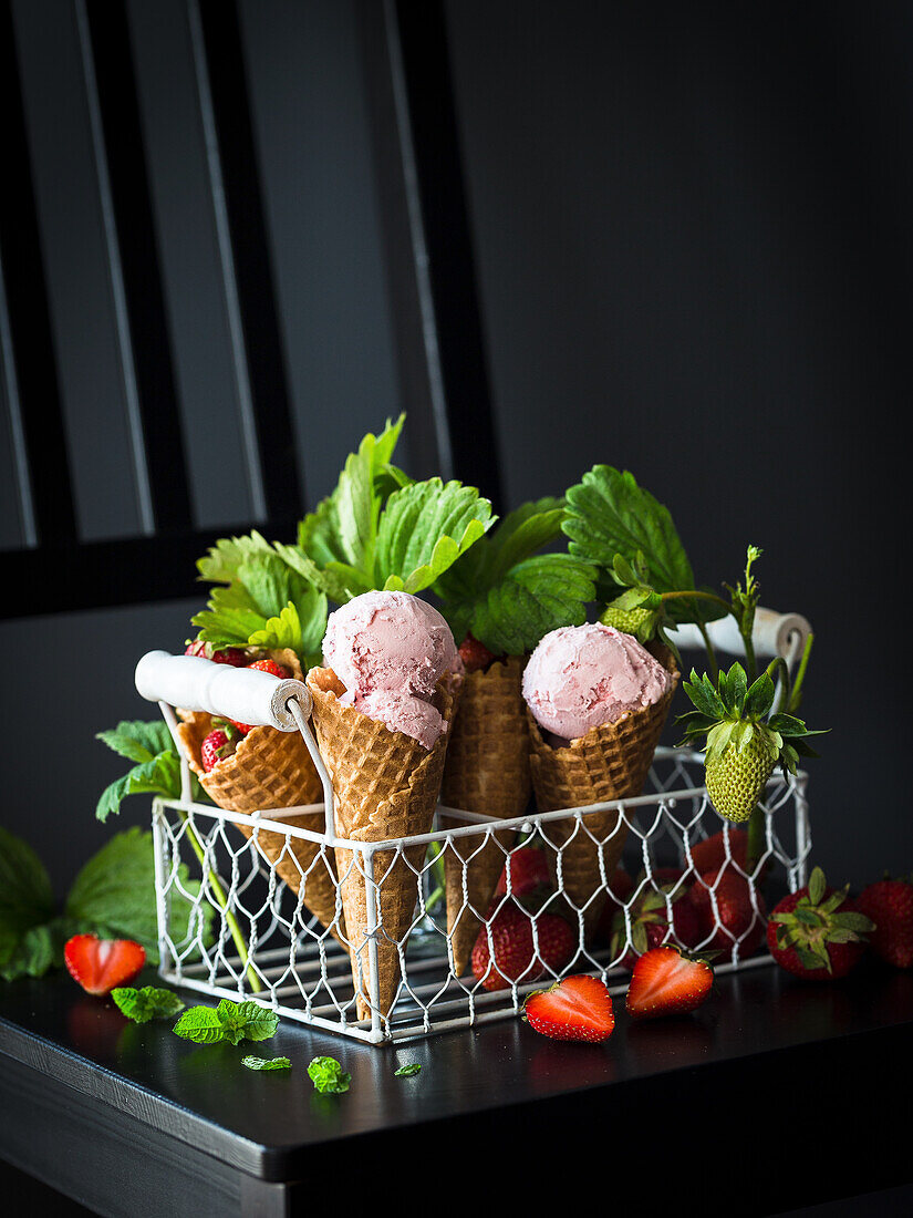 Strawberry ice cream in cones and fresh strawberries in a wire basket