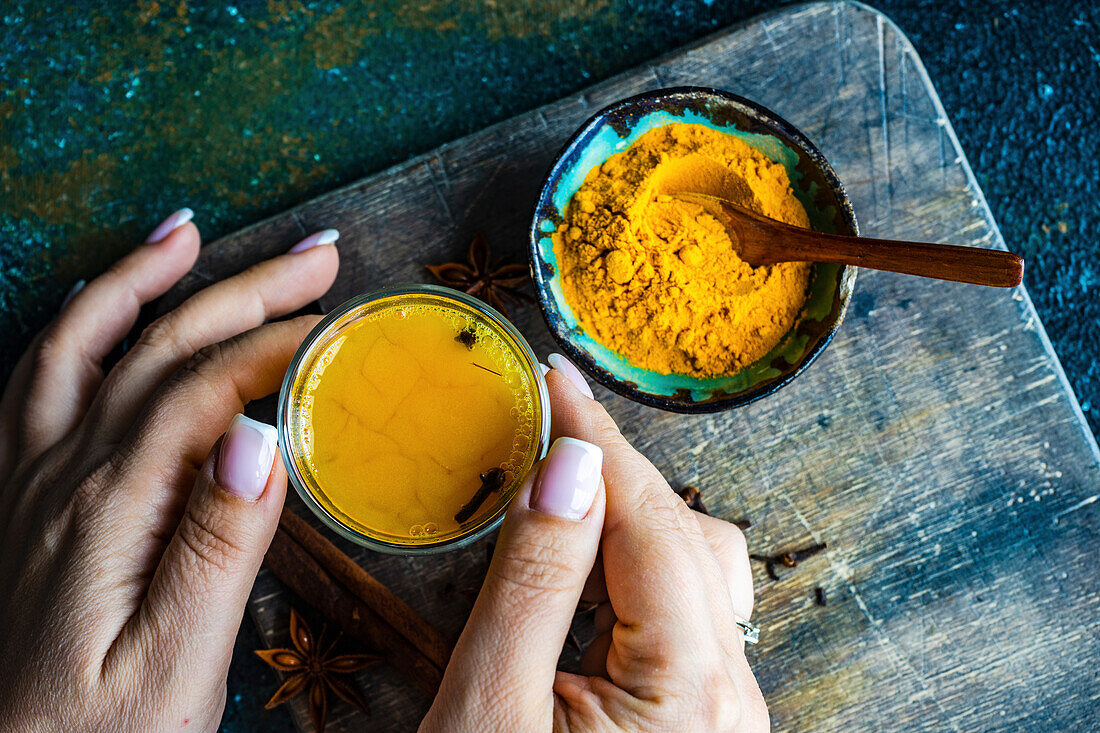 Spiced turmeric moon milk drink in the glass in woman hands on stone table