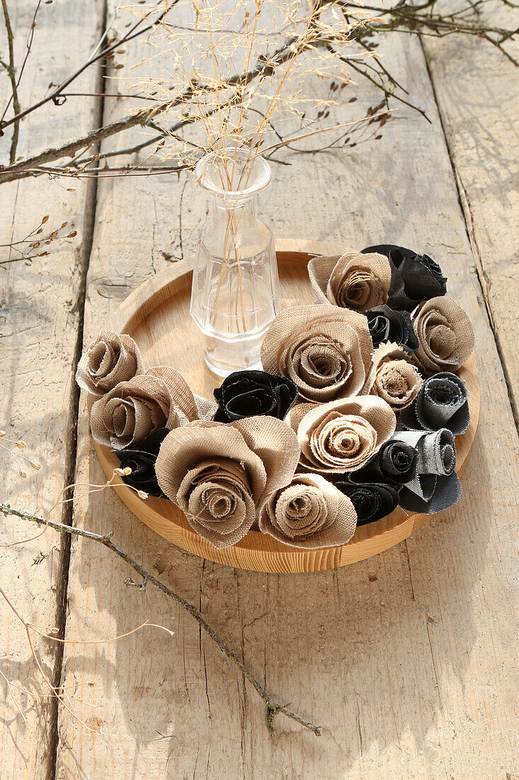 Beige and grey fabric roses on round wooden plate