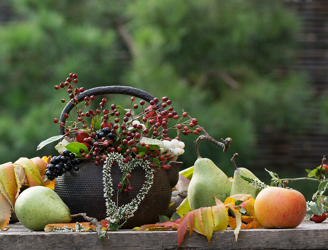 Old metal teapot with rose hips, privet, snowberry and heart of heather